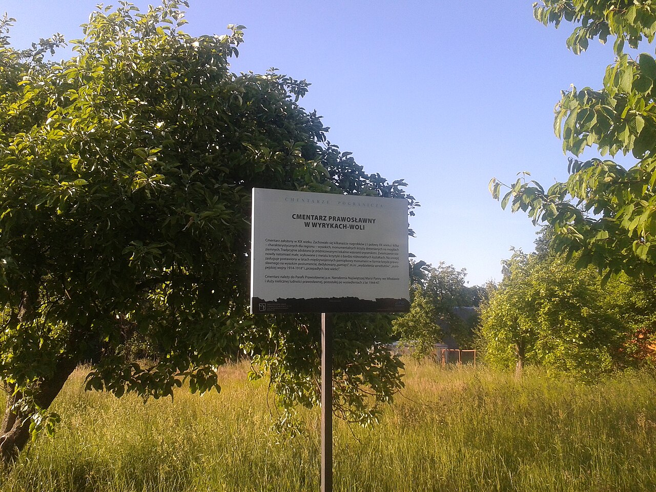 Tablica informacyjna przy wjeździe na cmentarz prawosławny w Wyrykach-Woli, 6 czerwca 2015 r. Zdjęcie archiwalne; nie przedstawia opisywanego zdarzenia. Plik bez zmian redakcyjnych; miniatura dopasowana do układu strony.